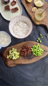 Fresh ingredients for an edamame avocado bowl, including avocado, green onions, edamame, mozzarella, and sesame tahini dressing.