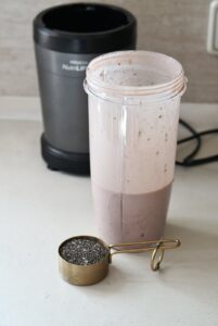 Adding chia seeds to a protein and coconut milk mixture in a blender jar