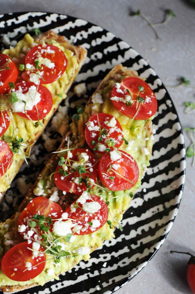 Close-up of avocado toast topped with feta cheese, cherry tomatoes and microgreens on toasted sourdough bread