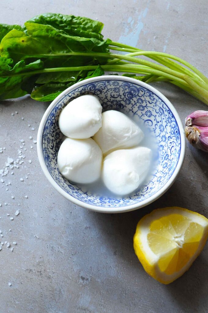 Fresh mozzarella balls with lemon, garlic, and leafy greens for a warm asparagus salad.