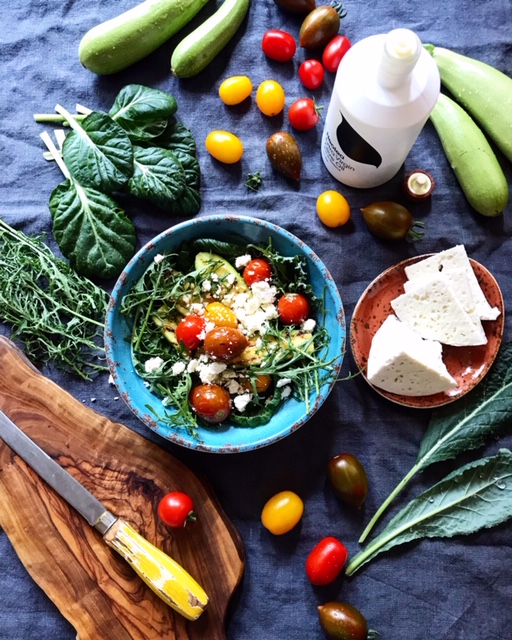Overhead view of warm grilled zucchini and cherry tomato salad with sheep cheese surrounded by fresh vegetables