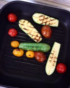 Zucchini and cherry tomatoes grilling on a hot grill pan until lightly charred