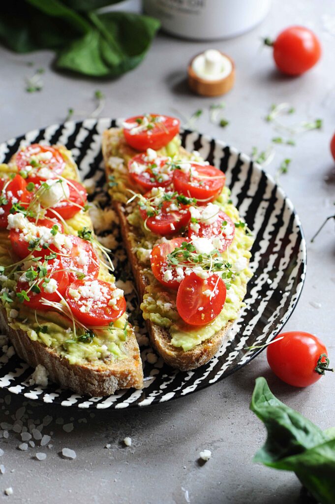 Healthy avocado toast with feta cheese, cherry tomatoes and microgreens on toasted sourdough bread