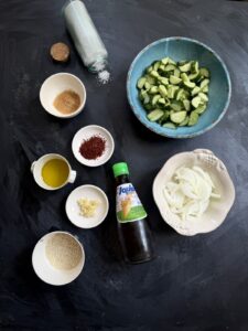 Ingredients for Korean Cucumber Salad (Oi Muchim), including cucumbers, onions, fish sauce, sesame oil, garlic, gochugaru, sugar, salt, and sesame seeds.