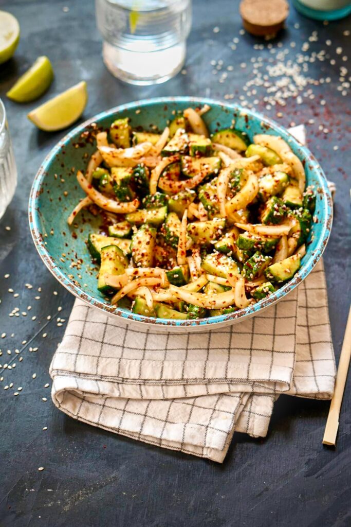 Korean Cucumber Salad (Oi Muchim) served in a blue bowl with sesame seeds, onions, and spicy gochugaru.
