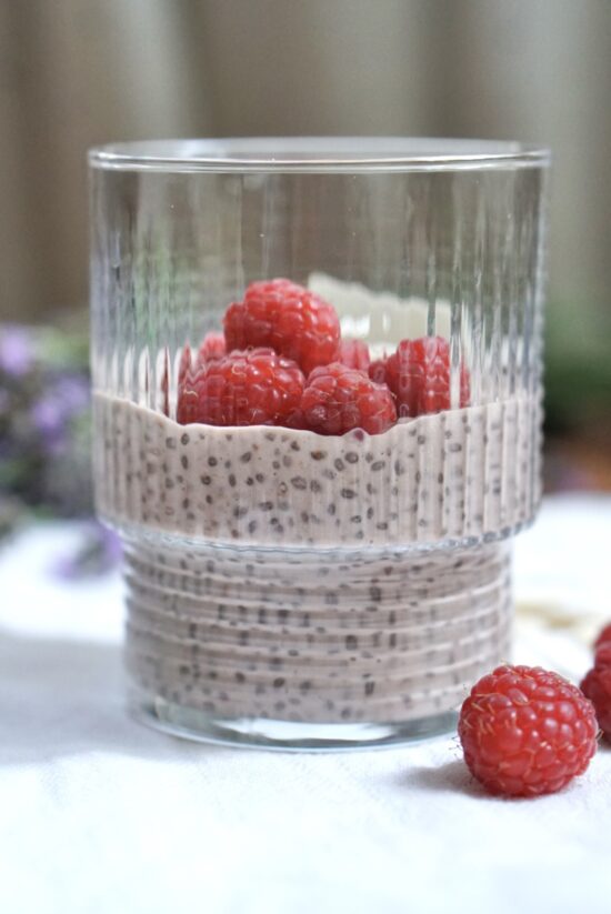 Protein chia pudding with coconut milk topped with fresh raspberries in a glass