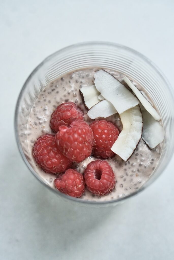 Top-down view of protein chia pudding with coconut milk, garnished with coconut flakes and raspberries