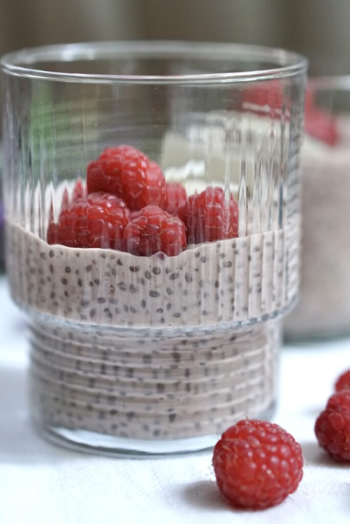 Side view of protein chia pudding in a glass topped with fresh raspberries