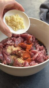 Minced garlic being added to beef strips already seasoned with soy sauce and spices