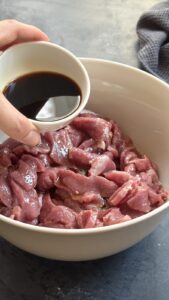 Soy sauce being poured over sliced raw beef in a bowl to start the marinade
