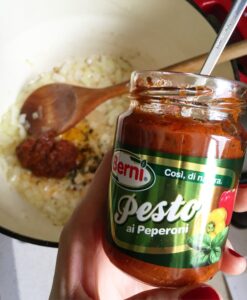 Red pepper pesto being added to sautéed onions for creamy tomato and red pepper soup.