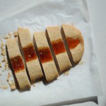 Sliced almond jam ribbon cookies arranged on parchment paper