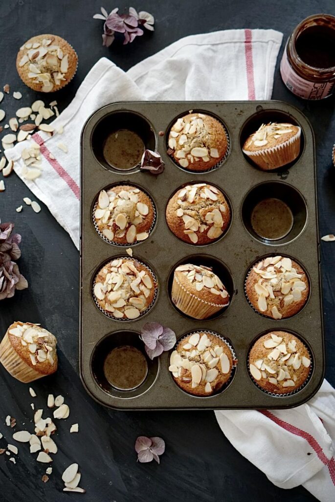 Almond-topped cherry muffins in a baking pan next to a jar of jam
