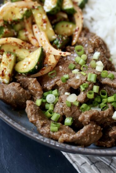 Close-up of beef stir-fry with soy sauce, green onions, white rice, and spicy cucumber salad.