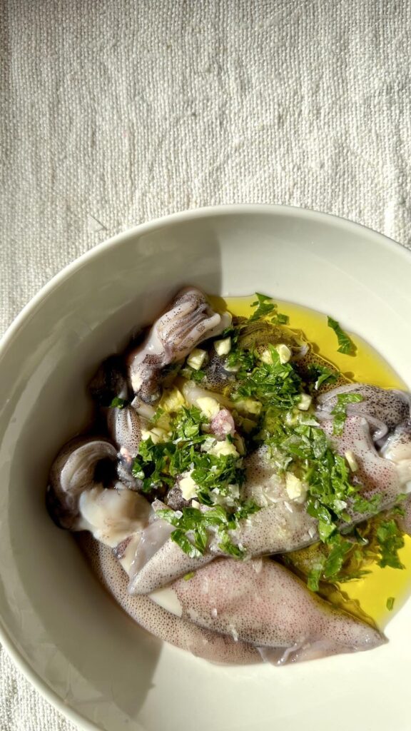 Cooked baby squid garnished with fresh parsley and a large lemon wedge on a white plate