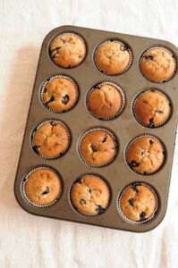 A muffin pan filled with 12 freshly baked blueberry lemon poppy seed muffins, golden brown on top