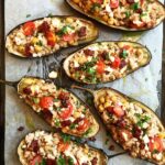 Baked eggplant boats stuffed with ground beef, chickpeas, cherry tomatoes, and feta cheese on parchment paper