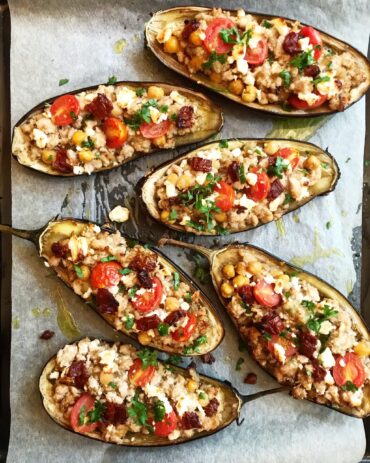 Baked eggplant boats stuffed with ground beef, chickpeas, cherry tomatoes, and feta cheese on parchment paper