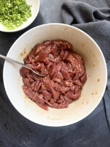 Sliced beef strips tossed in a soy sauce marinade with garlic and spices in a bowl