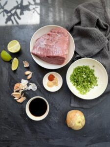 Overhead flat lay of beef stir-fry ingredients including sirloin steak, garlic, green onions, yellow onion, soy sauce, and spices