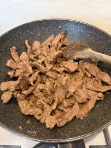 Thin beef strips browning and caramelizing in a hot skillet after the marinade has cooked down
