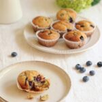 Blueberry lemon poppy seed muffins served on a table with fresh flowers and scattered blueberries