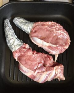 Thick bone-in steaks sizzling in a hot grill pan on the stovetop to develop a browned crust.