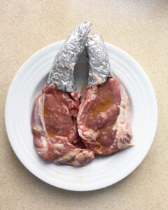 Raw bone-in steaks generously seasoned with kosher salt, black pepper, and olive oil, ready for cooking.