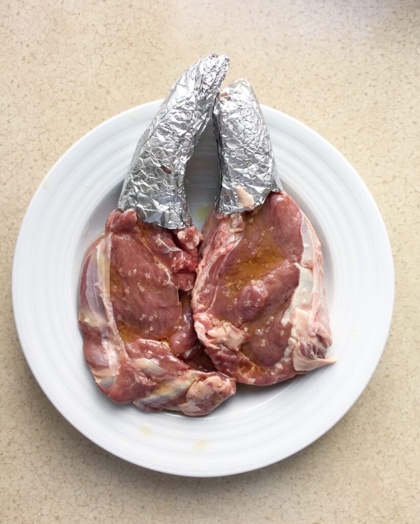Raw bone-in steaks generously seasoned with kosher salt, black pepper, and olive oil, ready for cooking.