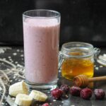 A tall glass of creamy pink cherry banana yogurt smoothie with honey