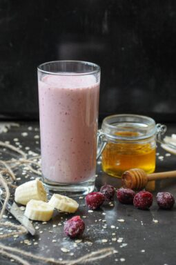 A tall glass of creamy pink cherry banana yogurt smoothie with honey