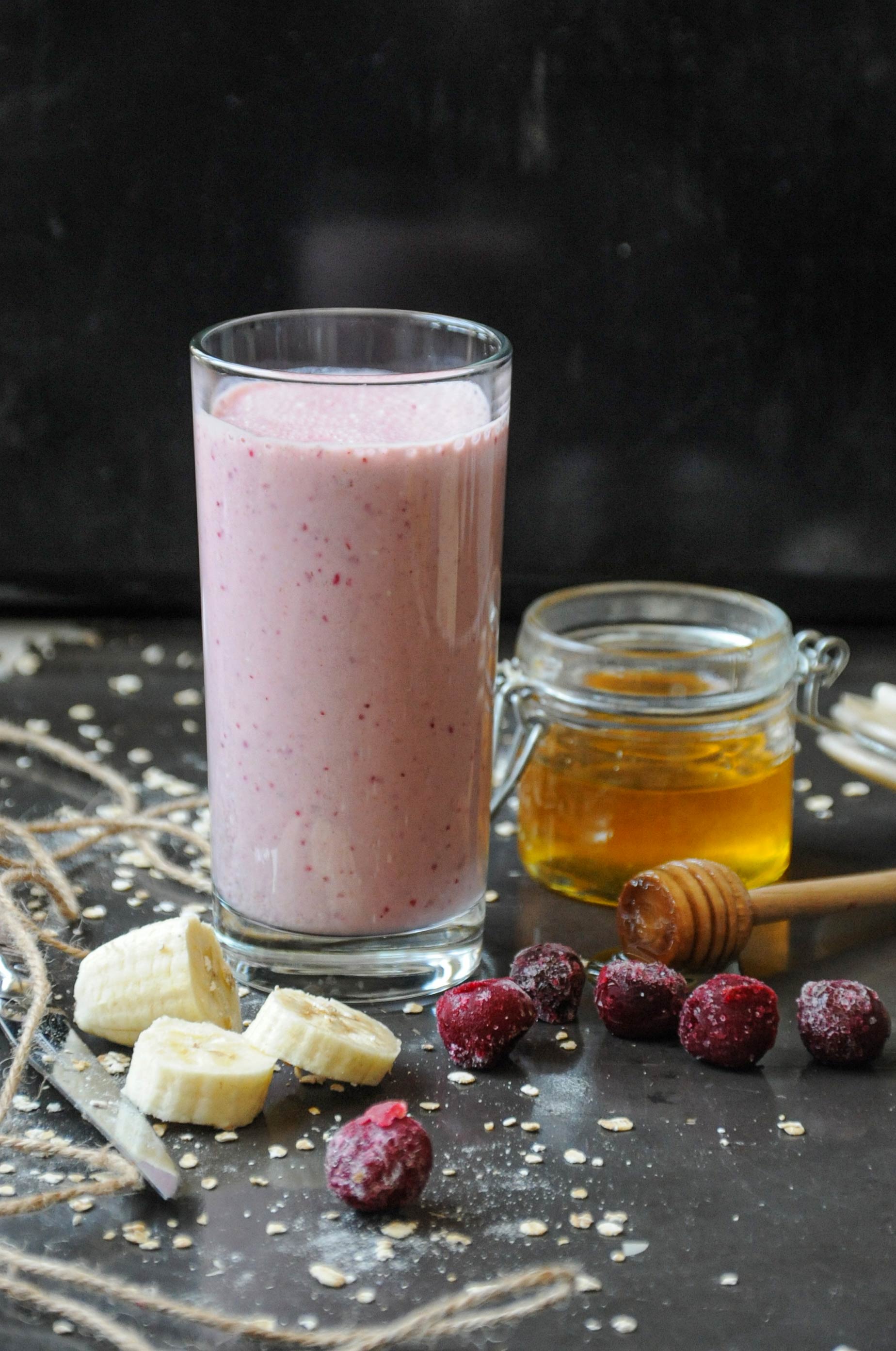 A tall glass of creamy pink cherry banana yogurt smoothie with honey