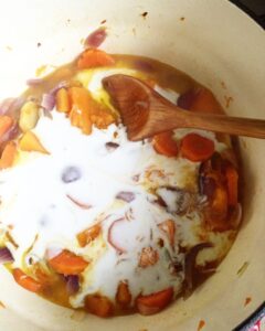 Pot of pumpkin soup simmering with coconut milk, carrots, and onions on the stove