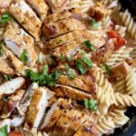 Close-up of creamy chicken pasta with tomatoes topped with sliced chicken and parsley