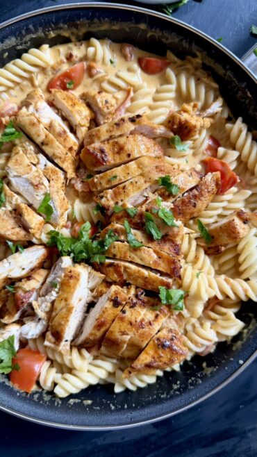 Close-up of creamy chicken pasta with tomatoes topped with sliced chicken and parsley