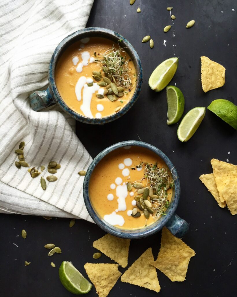 Bowls of creamy coconut pumpkin soup with ginger, served with lime wedges and tortilla chips