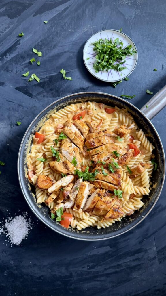 Skillet of creamy chicken pasta with fusilli, sliced chicken, tomatoes, and fresh herbs