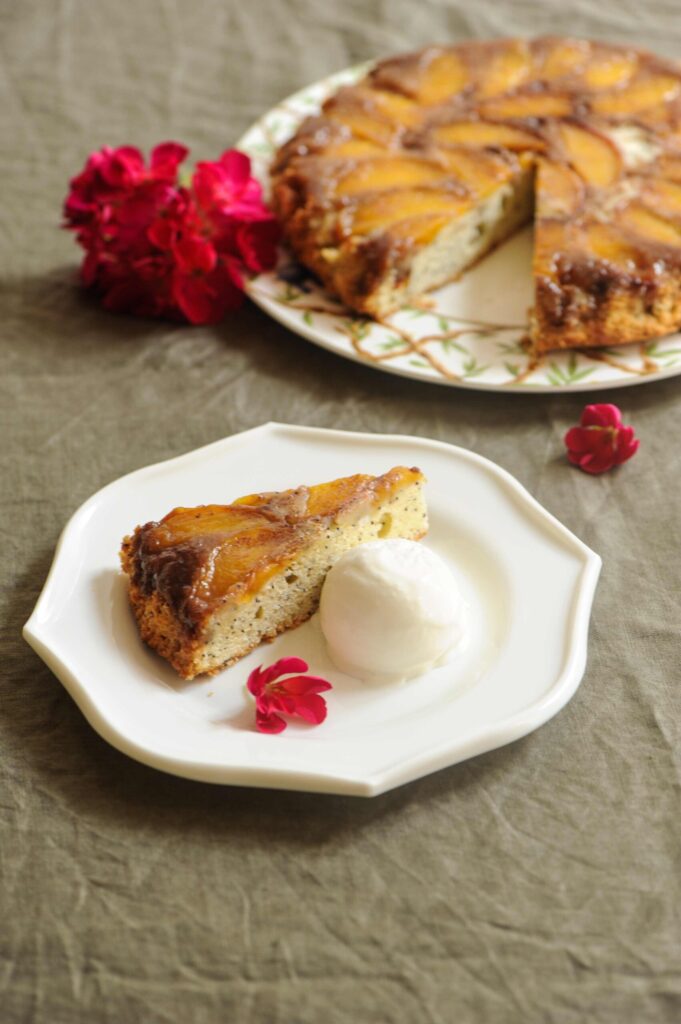 Close-up of a moist slice of peach upside-down cake with cinnamon and poppy seeds on a plate.