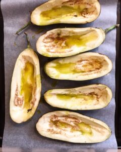 Halved eggplant shells brushed with olive oil on a parchment-lined baking sheet