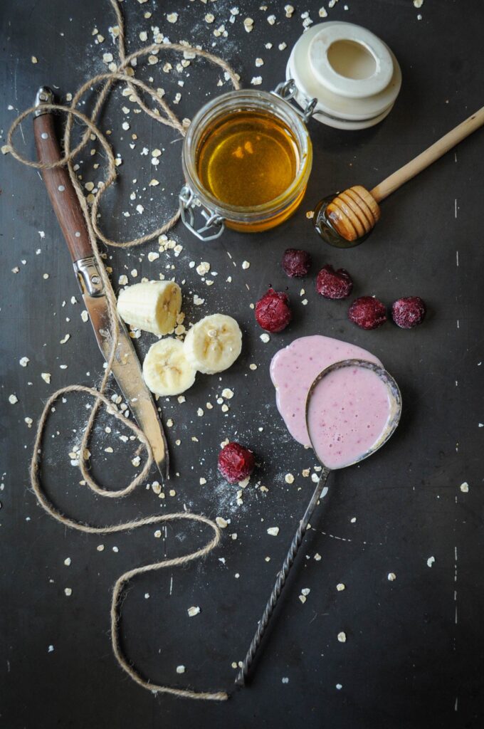 Ingredients for making a cherry banana yogurt smoothie including frozen cherries, sliced banana, drinkable yogurt, and honey