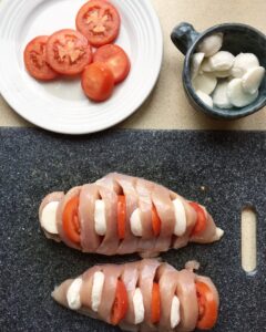 Close-up of raw chicken breast stuffed with sliced tomatoes and mozzarella before baking