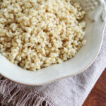 Fluffy cooked bulgur wheat in a light ceramic bowl on a fringed linen napkin.