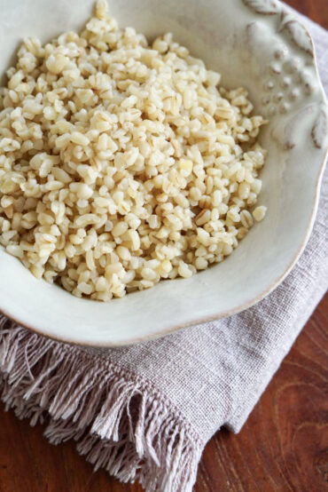 Fluffy cooked bulgur wheat in a light ceramic bowl on a fringed linen napkin.