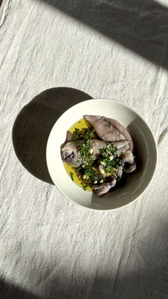 Overhead view of grilled baby squid drizzled with olive oil and chopped fresh parsley on a white plate