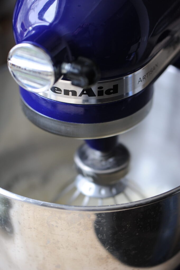 A blue KitchenAid stand mixer whipping batter for a lemon ginger bundt cake in a stainless steel bowl.