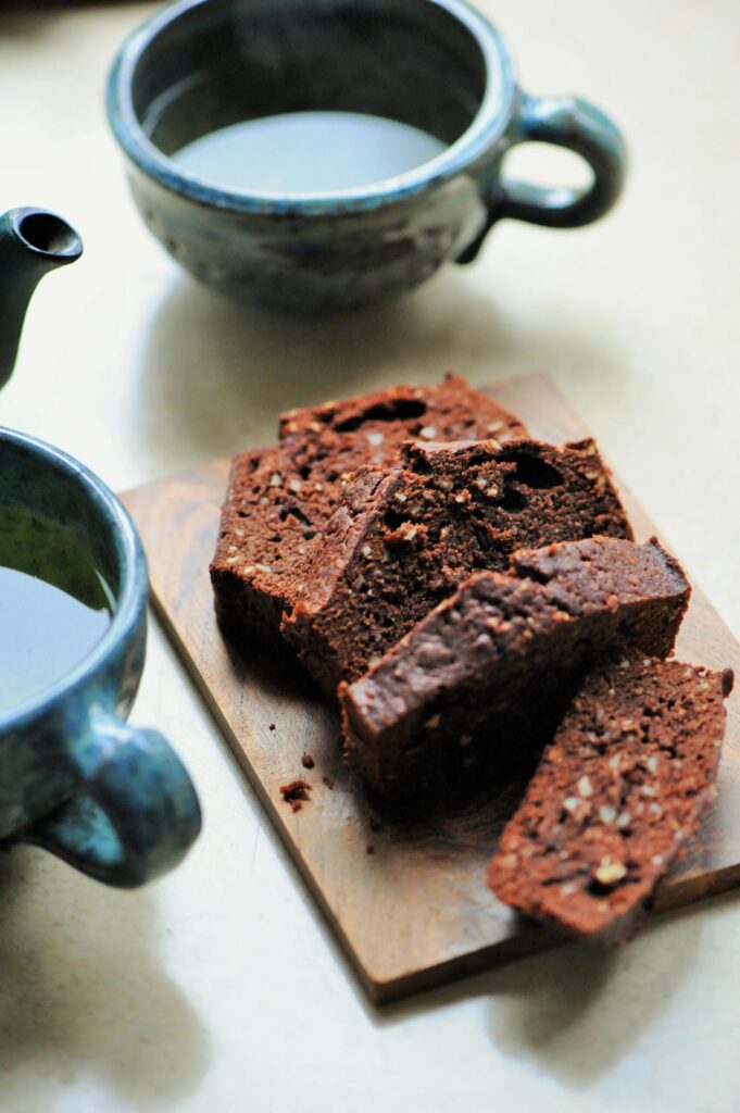 Sliced moist chocolate almond loaf cake on a wooden board next to ceramic teacups