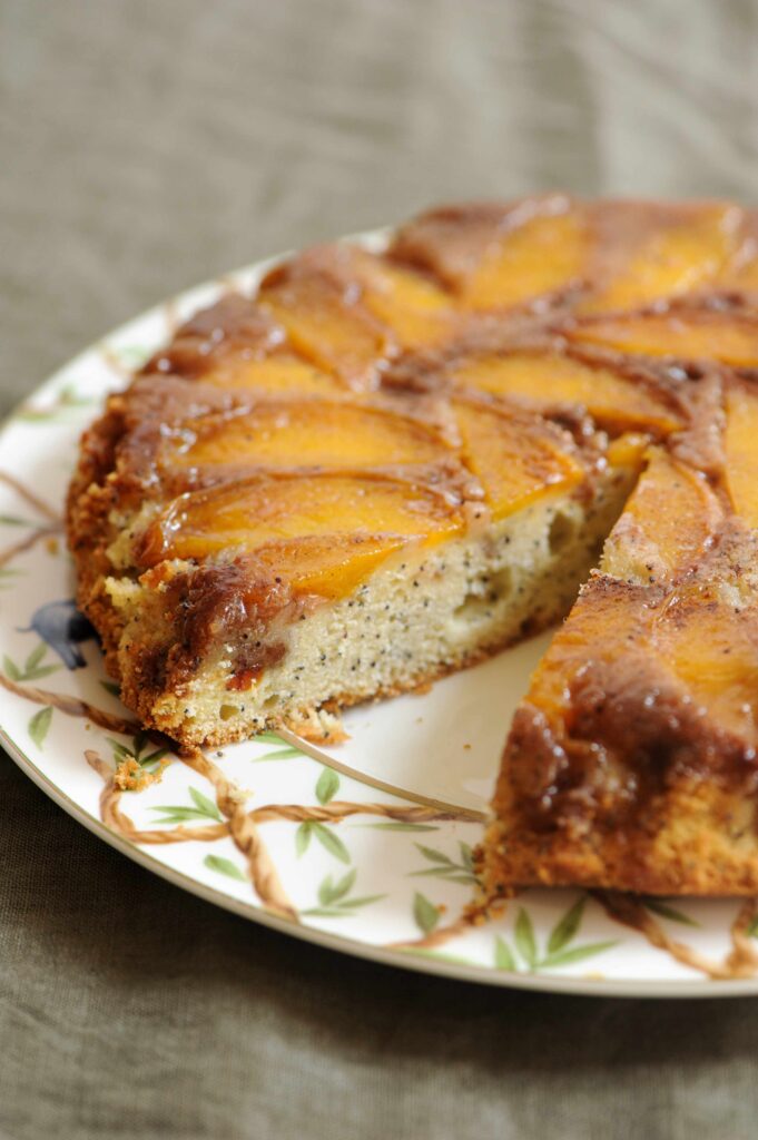 Freshly baked peach upside-down cake topped with caramelized peaches and poppy seeds on a serving plate.