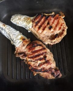 Two pan-seared bone-in steaks with distinct grill marks resting in a dark cast-iron grill pan.