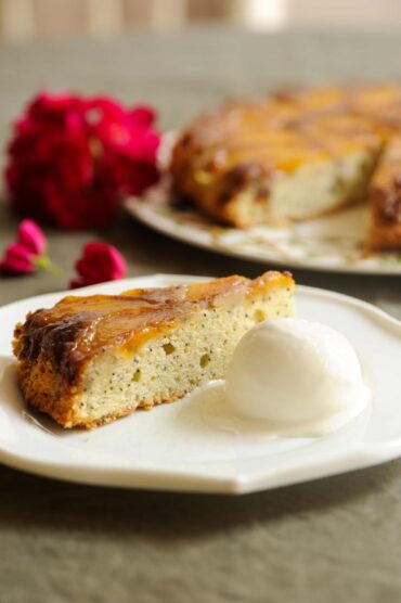 A slice of warm peach upside-down cake with poppy seeds served on a plate alongside a scoop of vanilla ice cream.