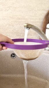 Rinsing bulgur wheat in a purple fine-mesh strainer under running tap water.